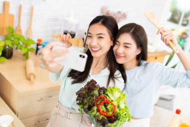 İki Asyalı aktif kadın mutfakta selfie çekiyor. Kadın sağlıklı yemek salatasıyla eğleniyor.