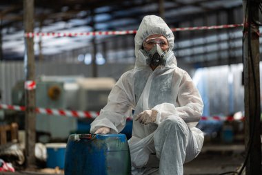 PPE koruyucu giysiler ve gaz maskeleri takan beyaz kadın işçiler, ellerinde eski benzin tankları tutuyorlardı..