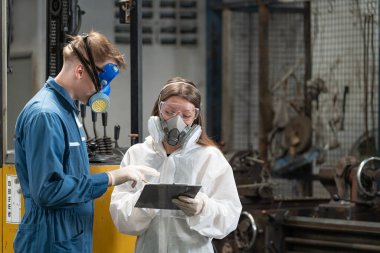 Acil kirlilik fabrikası konsepti. Tamirci, mekanik tulum ve gaz maskesi takan mühendis kollarını kavuşturarak kameraya bakar..