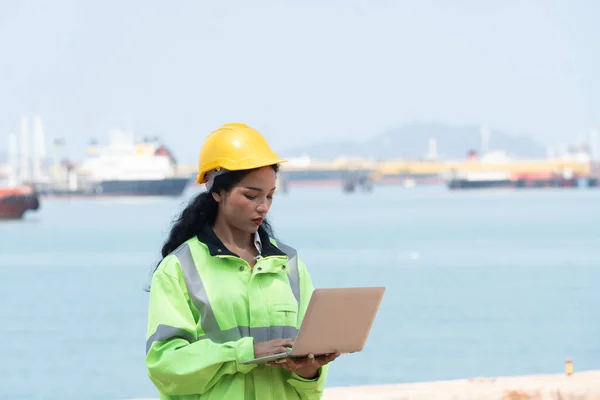 stock image Asian female engineer holding laptop with ocean ship background.