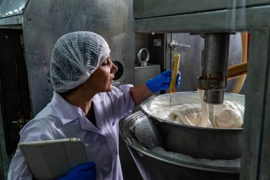 Yiyecek fabrikasında çalışan, koruyucu giysiler ve eldivenler giyen bir kadın.