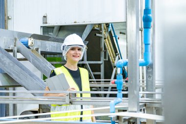 Ağır bir sanayi fabrikasında dururken beyaz kask takan kadın endüstriyel mühendis..