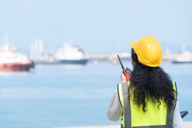 Asian Female Engineer Holding Walkie-Talkie with Marine Ship Background.