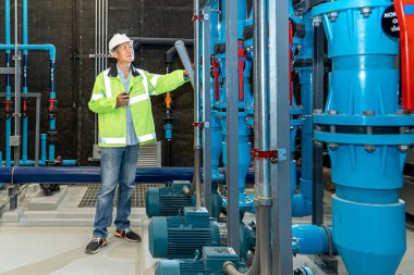 Korumalı üniformalı Asyalı işçi ve kasketli. Boru fabrikasındaki sıcaklığı ölçmek için tablet kullanıyor.