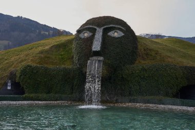 Wattens, Avusturya - 18 Mart 2023 - Swarovski Kristallwelten 'deki gölete su tüküren dev başlı bir çeşme                               