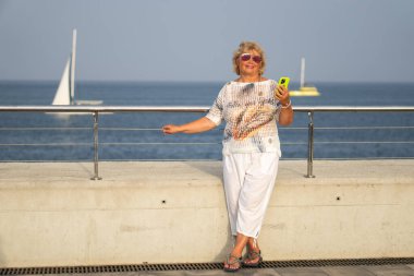 Kumsala yakın güneşli bir günde, beyaz saçlı çekici yaşlı bir bayan akıllı telefonundan mesajları okurken gülümsedi. Son sınıf öğrencisi cep telefonunu tutarken boş zamanının ve tatilinin tadını çıkardı.