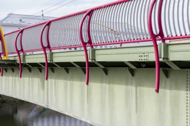 Otomobil ve yaya köprüsünün nehir üzerindeki kırmızı metal çitleri..