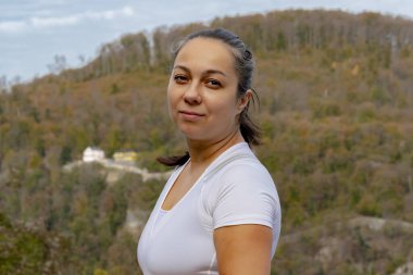 40-45 yaşlarında, dağların ve ormanların bulanık arka planında beyaz tişörtlü güzel bir esmer kadının portresi. Kavram: aktif eğlence, turizm ve seyahat.