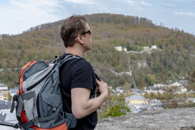 Omzunda sırt çantası olan bir erkek turist güzel bir dağ manzarasının ve eski şehir mimarisinin arka planına karşı. Konsept: turizm ve seyahat, emeklilik tatilleri.