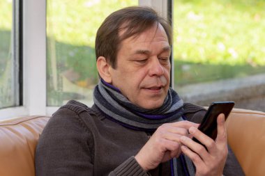 Yaşlı bir adam kanepede otururken akıllı bir telefonla yazı yazıyor..