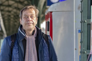 45-50 yaşlarında yaşlı bir adamın sokak portresi tren istasyonundaki bir bilet otomatının arka planına karşı..