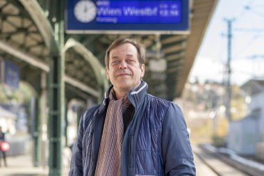 45-50 yaşlarındaki gülümseyen yaşlı bir adamın sokak portresi tren ya da tren istasyonunun bulanık arka planında tren ya da tren bekliyor..