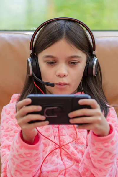 Dziewczyna Entuzjazmem Gra Grę Smartfonie Słuchawkami Mikrofonem Siedzącym Skórzanym Krześle — Zdjęcie stockowe