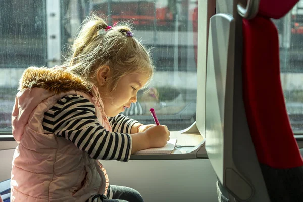 一个漂亮的小女孩在火车上的折叠桌上动情地画画 — 图库照片