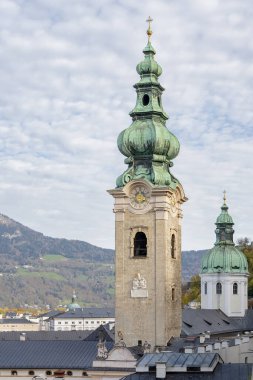 Avusturya 'nın tarihi bir şehrinde eski bir saat kulesi Salzburg' daki bir dağ manzarasının arka planına karşı..