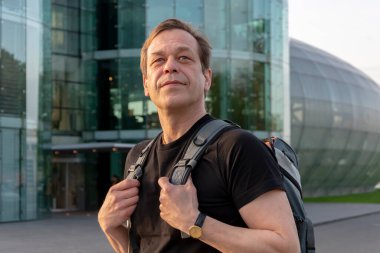 45-50 yaşlarında, modern cam bir binada sırt çantalı yaşlı bir turist. Konsept: turizm ve seyahat, hava ulaşımı ve havaalanından kalkış.