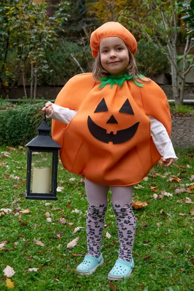 a girl in a pumpkin costume for Halloween with a lantern in her hand against the background of nature.