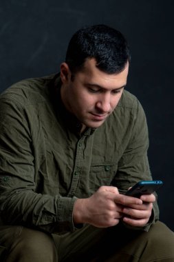 30-35 yaşlarındaki ciddi bir adamın portresi, akıllı telefon ya da siyah arka planda mesajlar yazıyor..