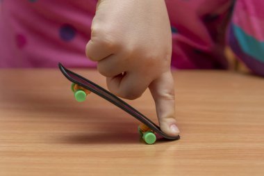 A child's hand does a fingerskate trick on a wooden table, close-up, selective focus.Finger training.