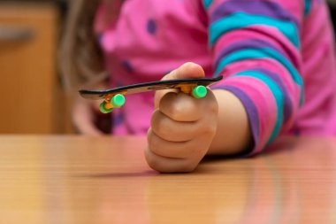 Fingerboard in a child's hand, wooden surface, close-up,