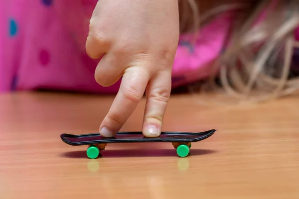 child\'s fingers on a fingerboard, wooden surface, close-up, selective focus. Fingerskate finger training.