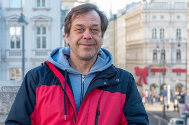 Street portrait of a smiling man 45-50 years old in a jacket on a blurry background of a European city.
