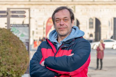Street portrait of an elderly man 45-50 years old in a jacket on a blurry urban background.