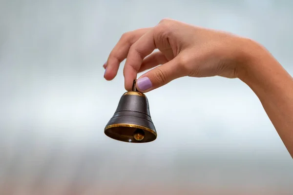 A small bell in the girl's hand on a neutral background, close-up, Concept: the first bell, a ringing bell.