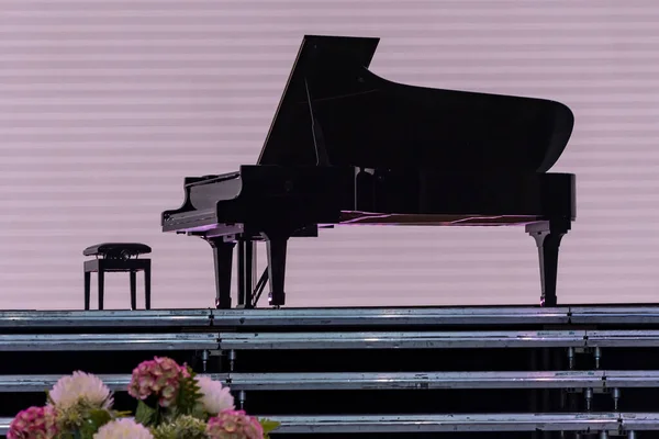A black piano and a chair on the podium of the stage, a bouquet of flowers.