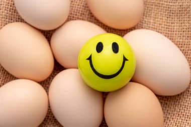 Tavuk yumurtalarının üzerinde gülen yüzlü bir top var. Kumaş bir arka plan..