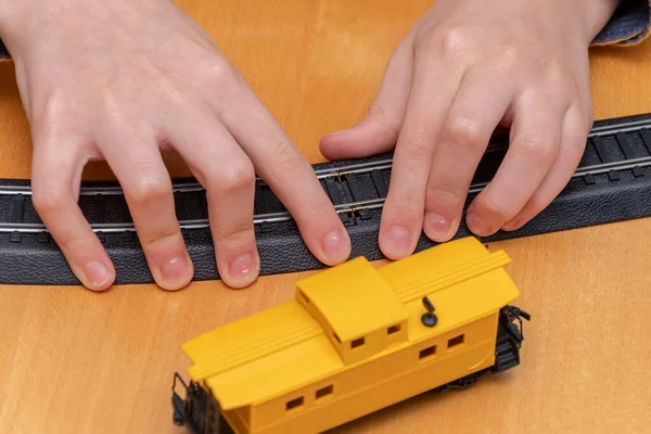 Children\'s hands collect rails from a toy railway with power supply, next to a toy trailer.