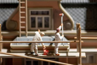 A scene of miniature figures, workers on wooden scaffolding painting and repairing the facade of the building.