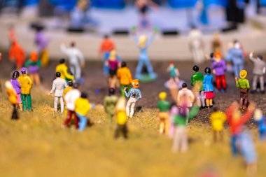 A scene of miniature figures at a concert, a crowd of people looking at the stage, a celebration in an open area.