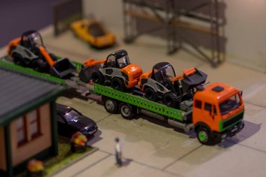 A cargo toy car carries forklifts in the back, there is a house, an urban landscape.