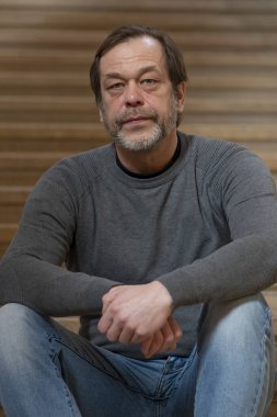 Portrait of an elderly man 45-50 years old with a gray beard sitting on the steps.
