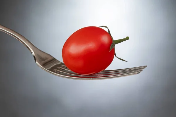 stock image Red cherry tomato with green leaves on a fork on a black background, selective focus.