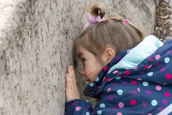 一个小女孩从水泥墙的孔里往外看 儿童的好奇心和对世界的了解 — 图库照片