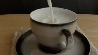 Süt, siyah arka planda, yavaş çekimde bir fincana dökülür..