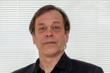 45-50 yaşlarında beyaz perdelerin açık arka planında takım elbiseli ciddi bir adamın portresi..