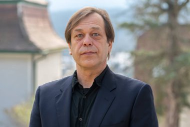 Tarafsız arka planda siyah takım elbiseli 40-50 yaşlarında bir adamın sokak portresi. Belki de sadece bir alıcıdır, bir aktör, bir emekli asker, bir şirket yöneticisi, şehir dışında yaşıyor..