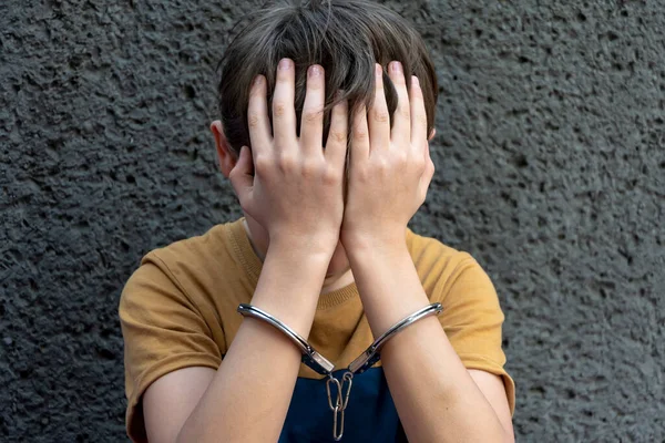 手錠をかけられた10歳の少年が灰色の背景に座っている 非行少年未成年者の刑事責任 青年犯罪グループや暴力団のメンバー — ストック写真