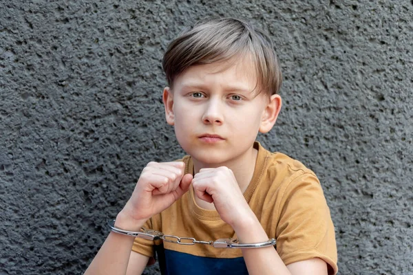 stock image A little criminal is handcuffed against a gray wall, an emotional portrait. Concept: juvenile delinquency, petty theft and theft, incarceration.