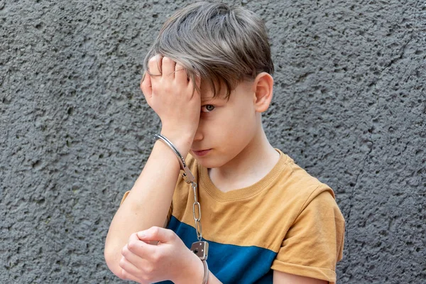 一个10岁的罪犯的画像 一个被手铐铐在灰墙上的男孩 少年犯罪 小偷小摸 — 图库照片
