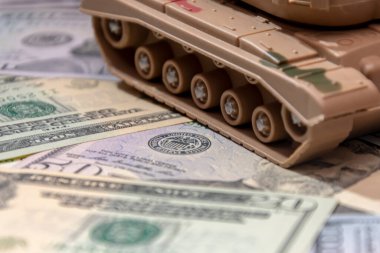 Oyuncak tankın tırtılları arka plandaki dağınık Amerikan dolarlarına karşı, yakın plan. Konsept: silah harcamaları, askeri yardım, silah ve mühimmat ticareti, para kredisi, Ukrayna 'da savaş.