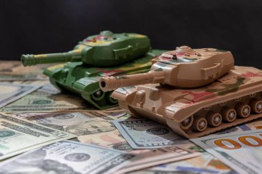 Oyuncak askeri tanklar, dağınık Amerikan doları, siyah arka plan. Konsept: silah harcamaları, askeri yardım, silah ve mühimmat ticareti, para kredisi, Ukrayna 'da savaş.