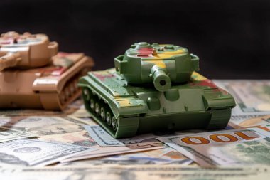 Oyuncak askeri tanklar, dağınık Amerikan doları, siyah arka plan. Konsept: silah harcamaları, askeri yardım, silah ve mühimmat ticareti, para kredisi, Ukrayna 'da savaş.