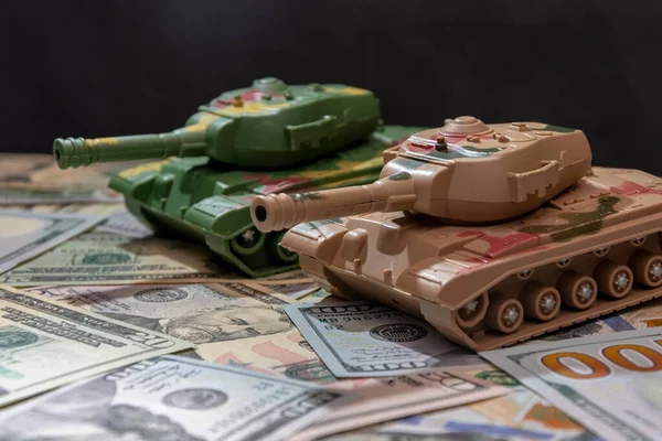 Oyuncak askeri tanklar, dağınık Amerikan doları, siyah arka plan. Konsept: silah harcamaları, askeri yardım, silah ve mühimmat ticareti, para kredisi, Ukrayna 'da savaş.