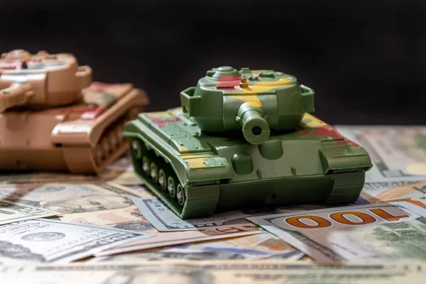 Toy military tanks, scattered american dollars, black background.  Concept: arms spending, military aid, arms and ammunition trade, money loan, war in Ukraine.
