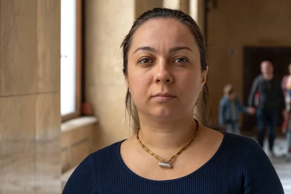 stock image Portrait of a serious woman 40-45 years old in a public building, indoors, against the background of windows and people passing by.