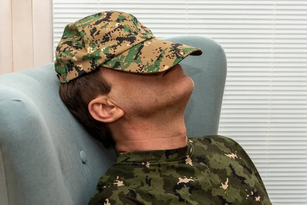 An elderly military man 45-50 years old covered his face with an army cap, sleeping sitting in an armchair. Concept: mental disorders in military personnel, treatment by a psychotherapist.